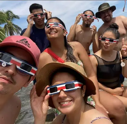 familia de ticos en la playa en la costa caribeña con lentes para eclipse solar con diseño de los colores de la bandera de costa rica